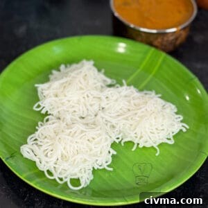 Freshly made idiyappam noodles served on a green plate with spicy curry in the background.