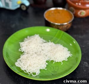 Fresh idiyappam noodles served on a green plate with curry in the background.