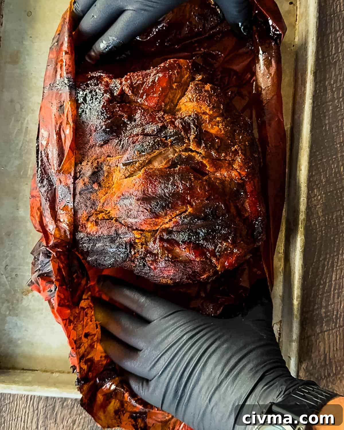 Gloved hands removing the wrapping from the rested pork shoulder.