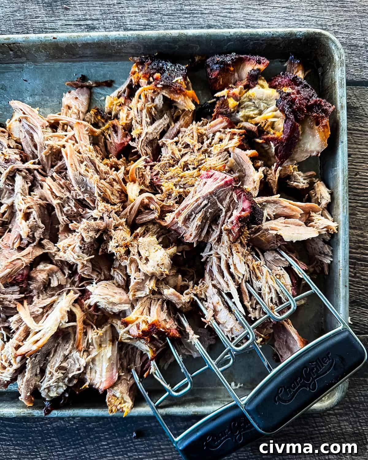 Pulled pork on a baking sheet with shredding forks.
