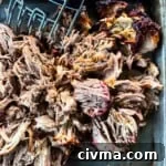 A pan filled with shredded pork cooked on a Pit Boss smoker being shredded with shredding forks.