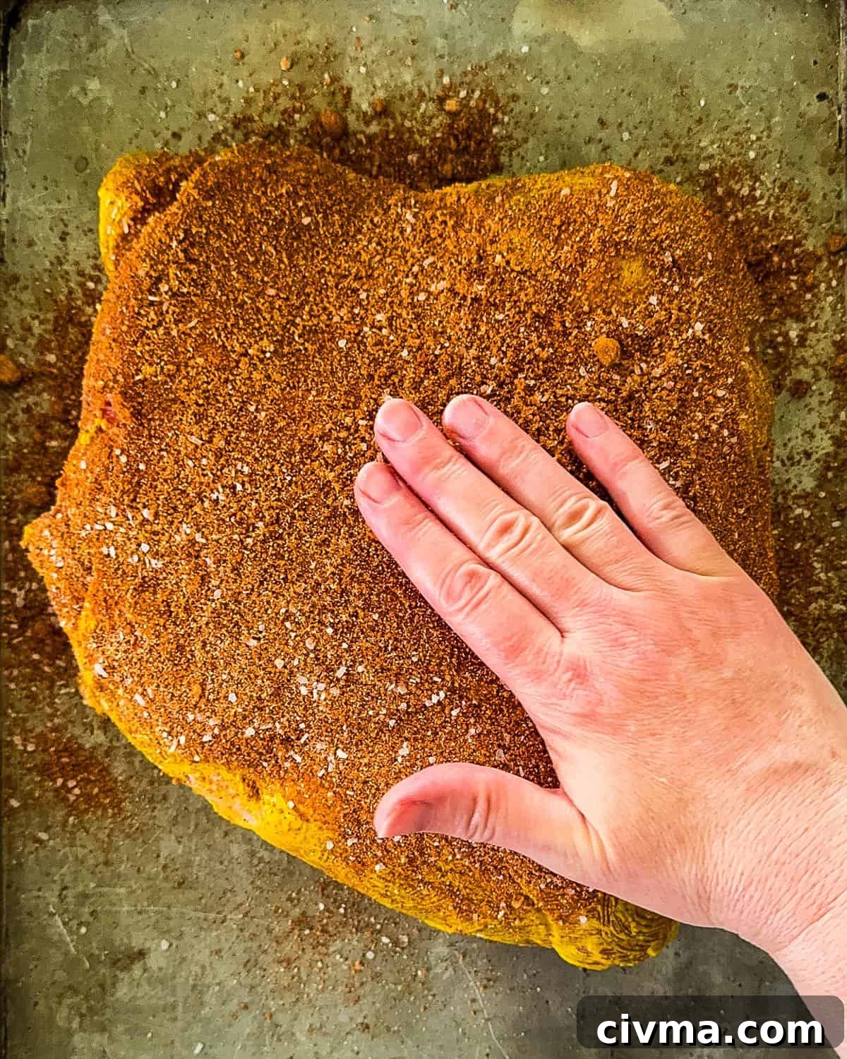 A hand rubbing spice rub into the pork shoulder.
