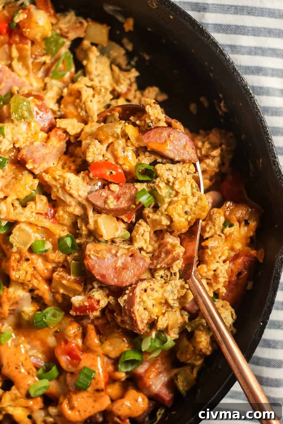 Close-up of a loaded Creole breakfast skillet with potatoes, sausage, eggs, peppers, and sauce.