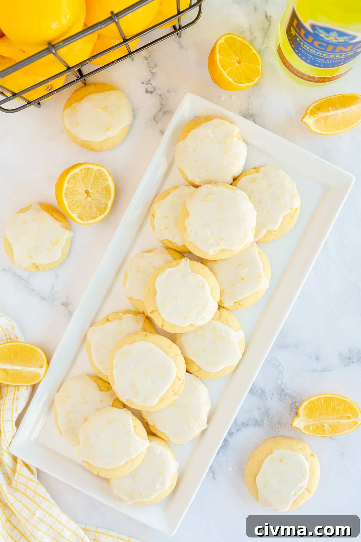 A tray of glazed Limoncello Cookies with a basket of lemons behind it shot from over the top.