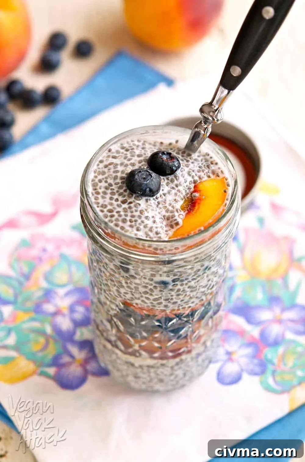 Blueberry peach chia parfait in a glass jar on a floral linen