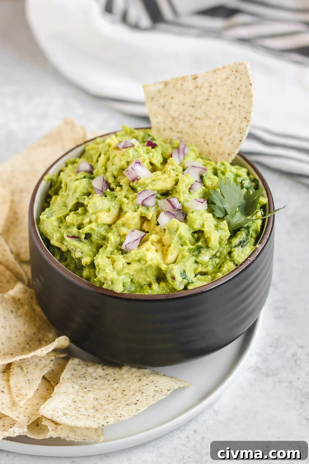 side view of guacamole in a black bowl with a chip sticking out of the quacamole