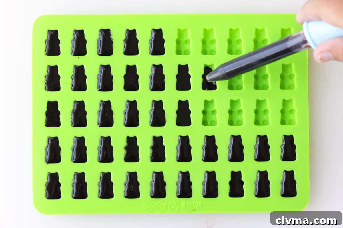 elderberry syrup being dropped into a silicone gummy bear mold with an eye dropper