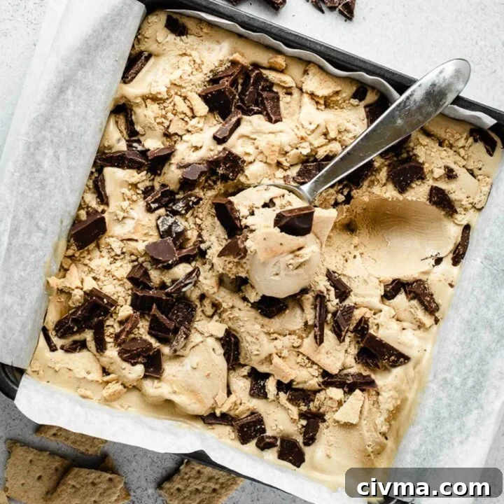 Ice cream scoop resting in a square baking dish filled with s'mores ice cream topped with chocolate chunks.