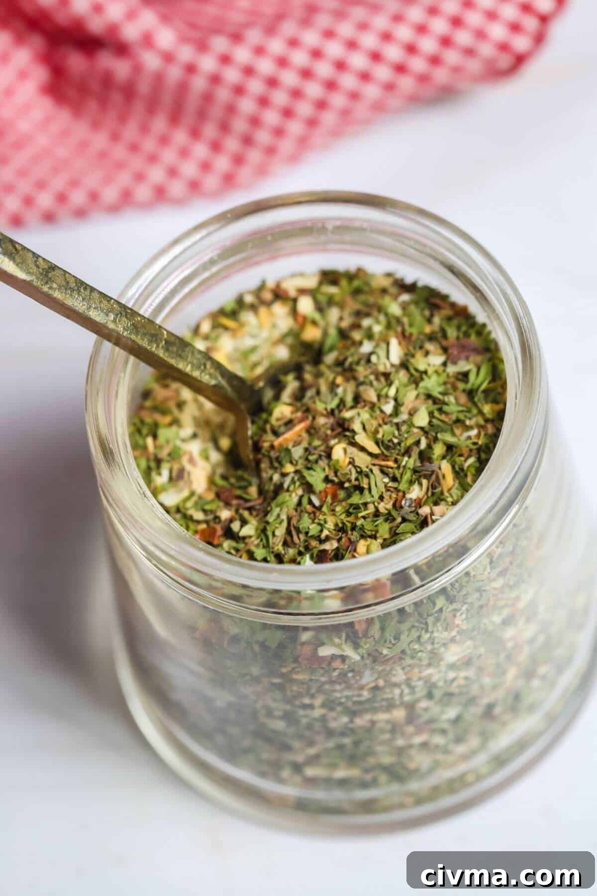 A jar of the spaghetti seasoning blend with a spoon in it.