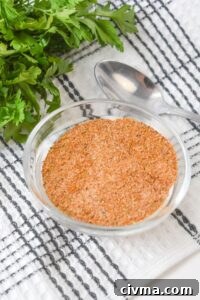 A bowl of meatloaf seasoning rests on a striped kitchen towel, surrounded by fresh parsley and a spoon.