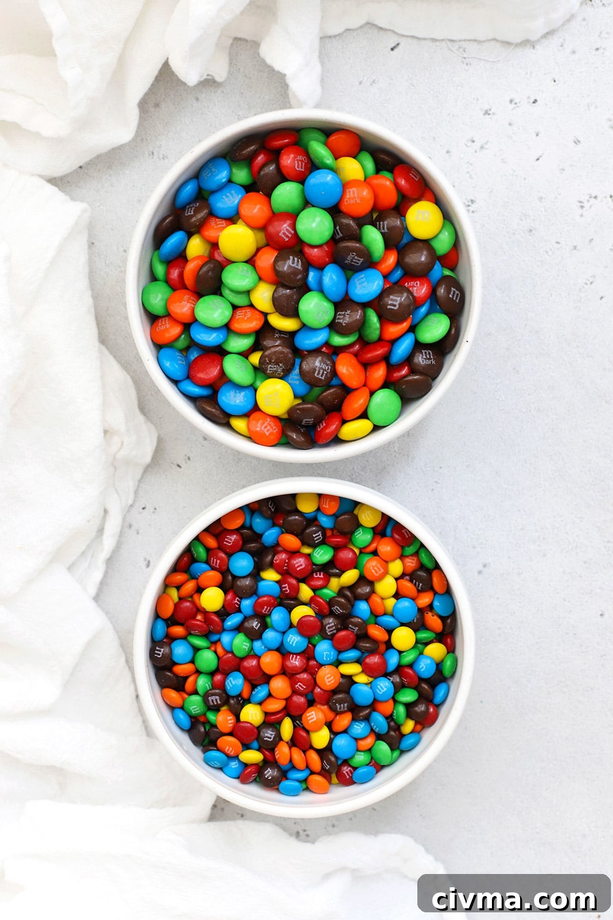 Overhead view of two bowls of M&Ms, one bowl of mini M&Ms and one bowl of regular M&Ms