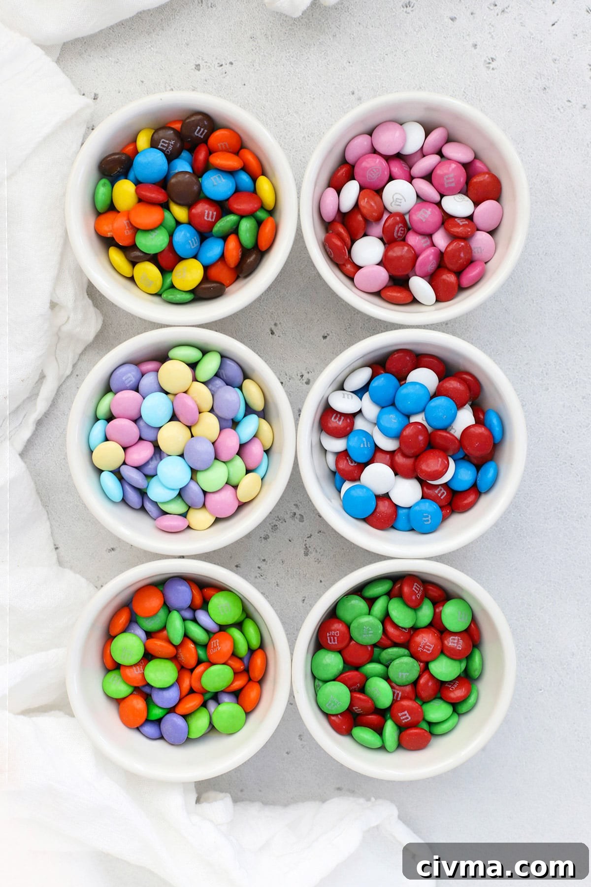 Overhead view of small bowls of holiday M&Ms including original, Valentine colors, red white and blue, Christmas colors, Halloween colors and pastel Easter colors