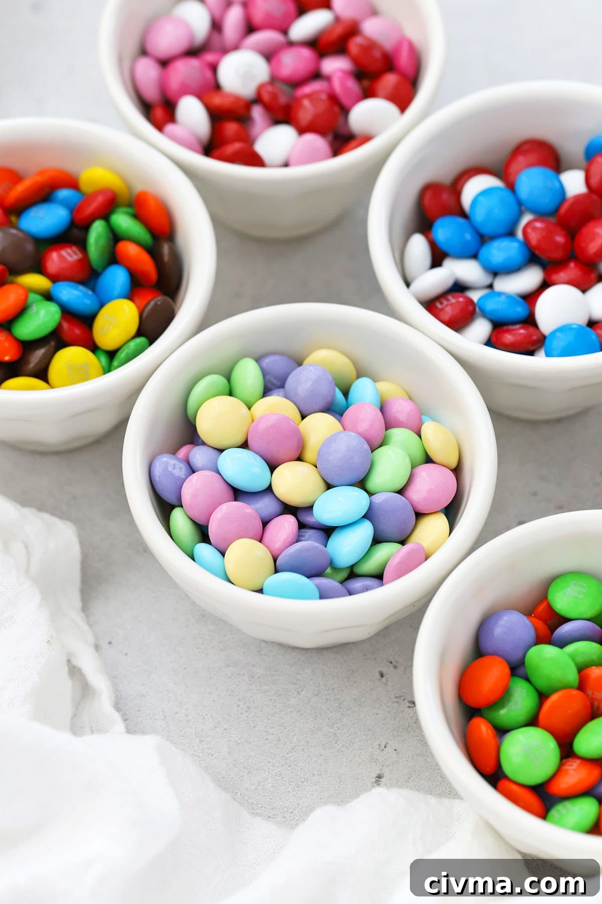 Front view of small bowls of holiday M&Ms including original, Valentine colors, red white and blue, Christmas colors, Halloween colors and pastel Easter colors