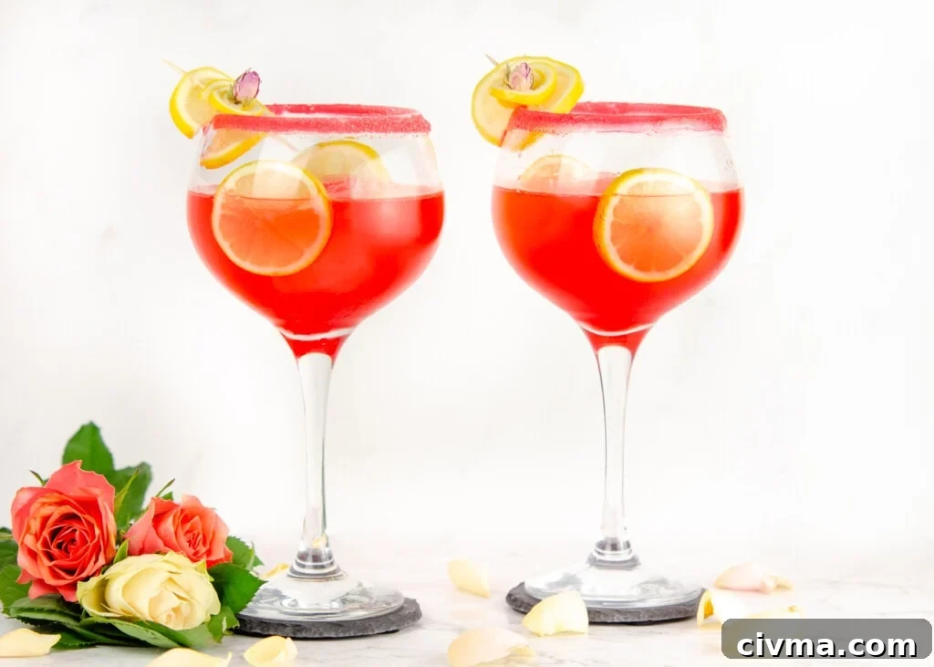 Pink Gin Fizz Cocktail served in sugar rim glasses garnished with lemon slices and cubes of ice in the glass and pink and white roses and white rose petals at the bottom of glass
