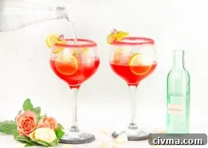 Pouring soda water into sugar rim glasses garnished with lemon slices and cubes of ice in the glass and pink and white roses at the bottom of glass and green bottle of soda water in the background