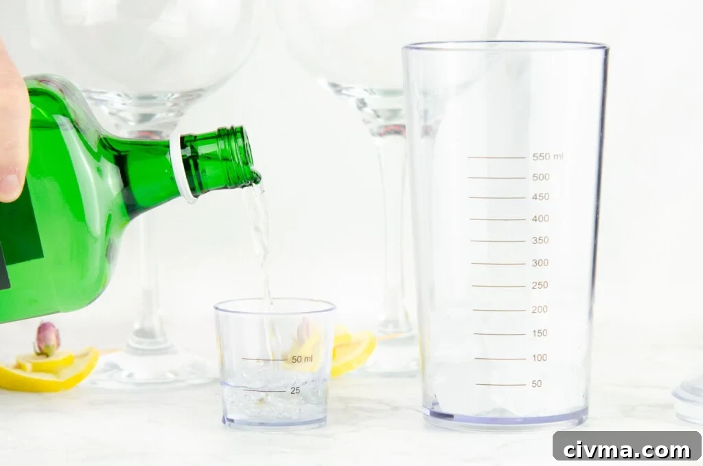 Pouring gin into a cocktail jigger to measure the gin for making the cocktail