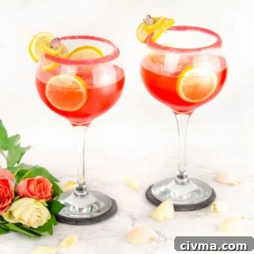 Pink Gin Fizz served in sugar rim glasses garnished with lemon slices and cubes of ice in the glass and pink and white roses at the bottom of glass