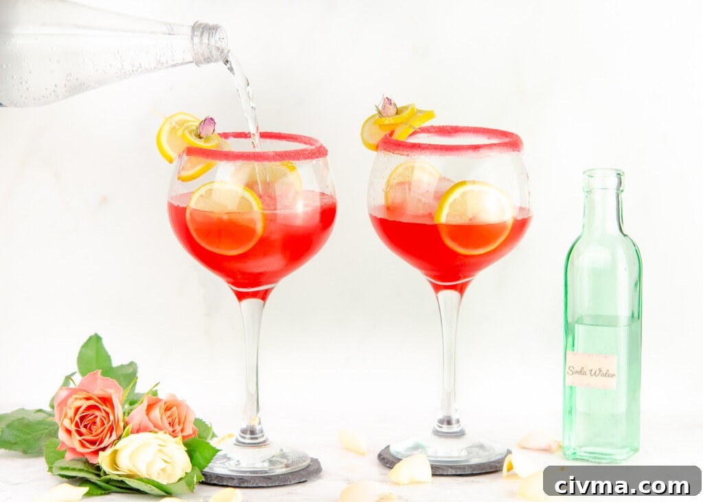 Pouring soda water into sugar rim glasses garnished with lemon slices and cubes of ice in the glass and pink and white roses at the bottom of glass and green bottle of soda water in the background