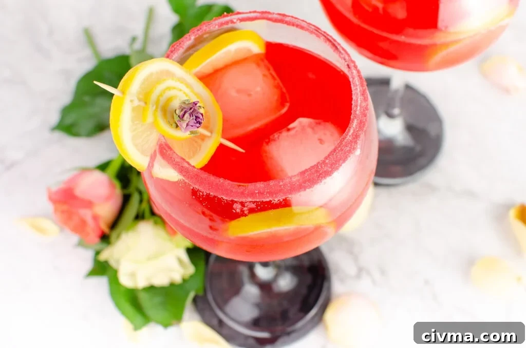 The best Pink Gin Fizz Cocktail served in a sugar rim gin glass garnished with a lemon slice and pink rose petal and pink and white roses at the bottom of the glass