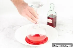 Dipping a gin glass rim into grenadine in a white bowl with a green bottle of grenadine in the background