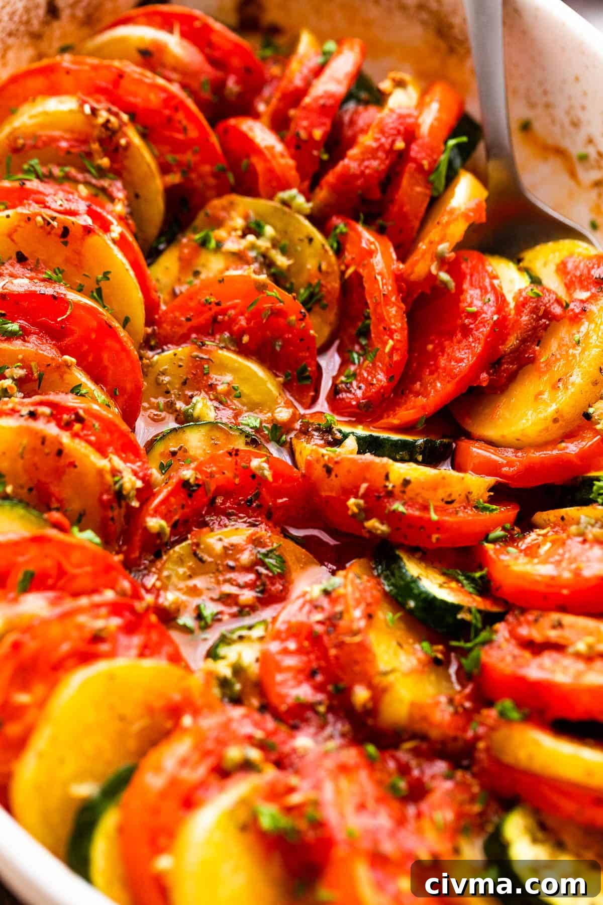 close up shot of zucchini slices, tomato slices, and potato slices arranged accordion style in a baking dish.
