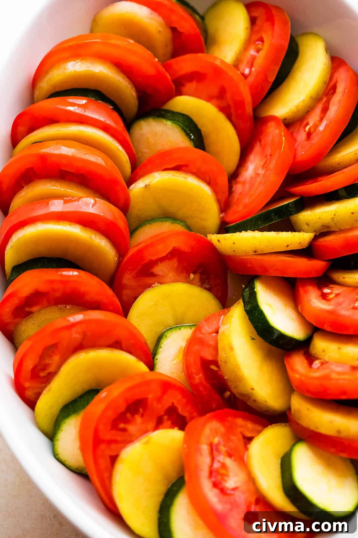 overhead shot of zucchini, tomato, and potato slices arranged accordion style in a baking dish.