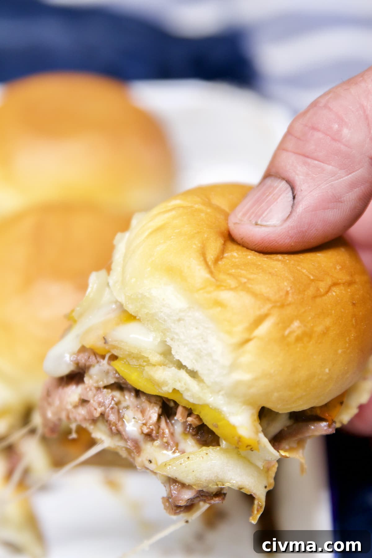 Philly Cheesesteak Sliders are a delicious meal or fun appetizer for cookouts and easy enough for any night of the week. Grilled steak, peppers and onions piled high on slider buns with melted provolone cheese is a delicious flavor combination! Grilled Philly Cheesesteak Sliders - held in hand.