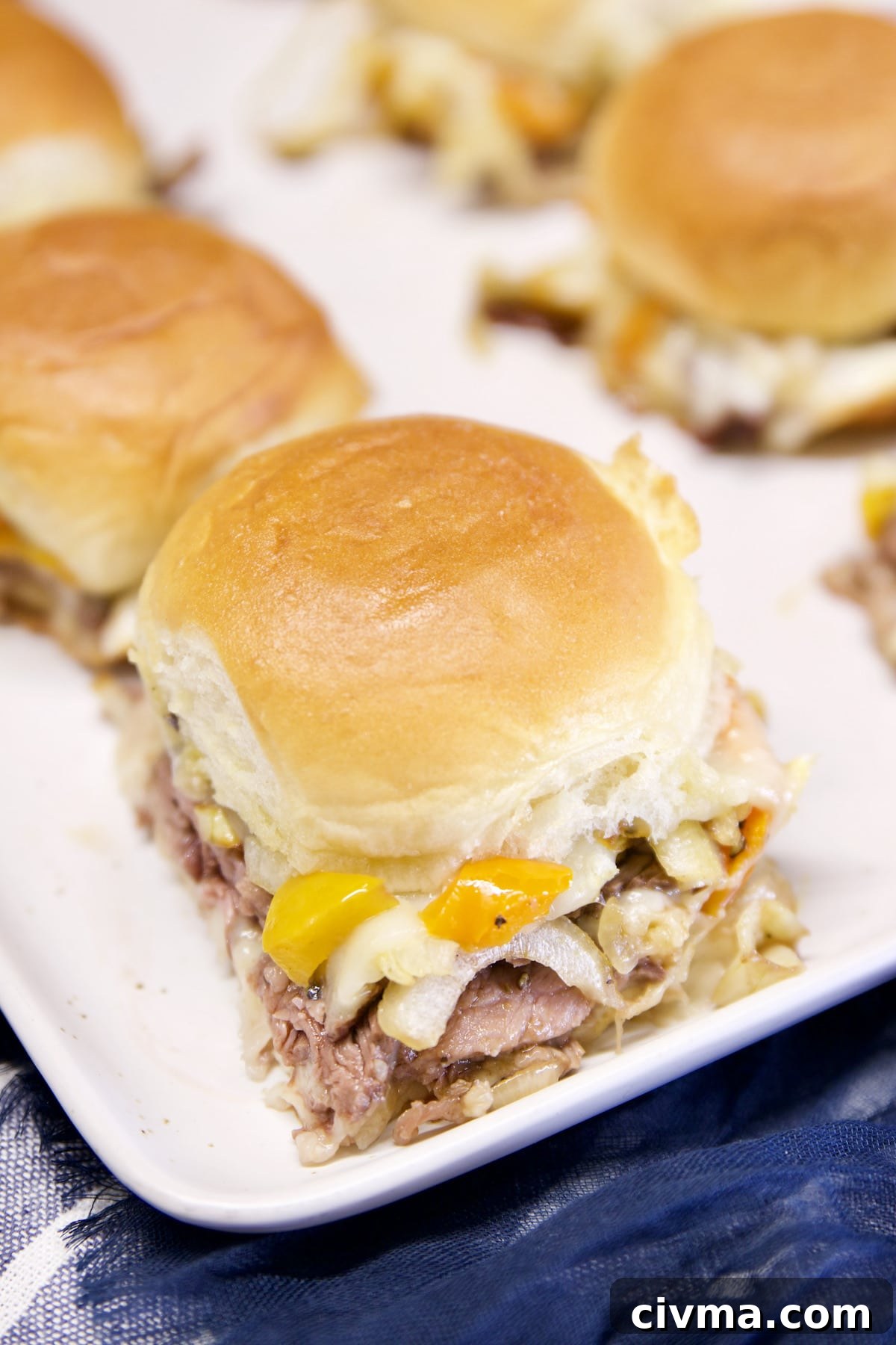 Sirloin steak sliders with peppers, onions and provolone cheese. Serving platter of cheesesteak sliders.
