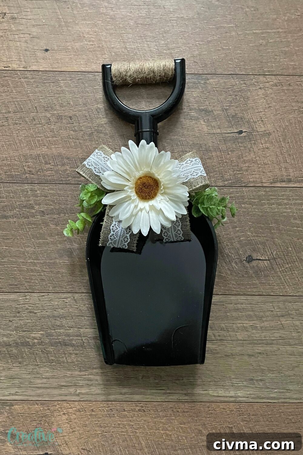DIY farmhouse door wreath made with a plastic shovel, greenery, burlap ribbon, and white flowers