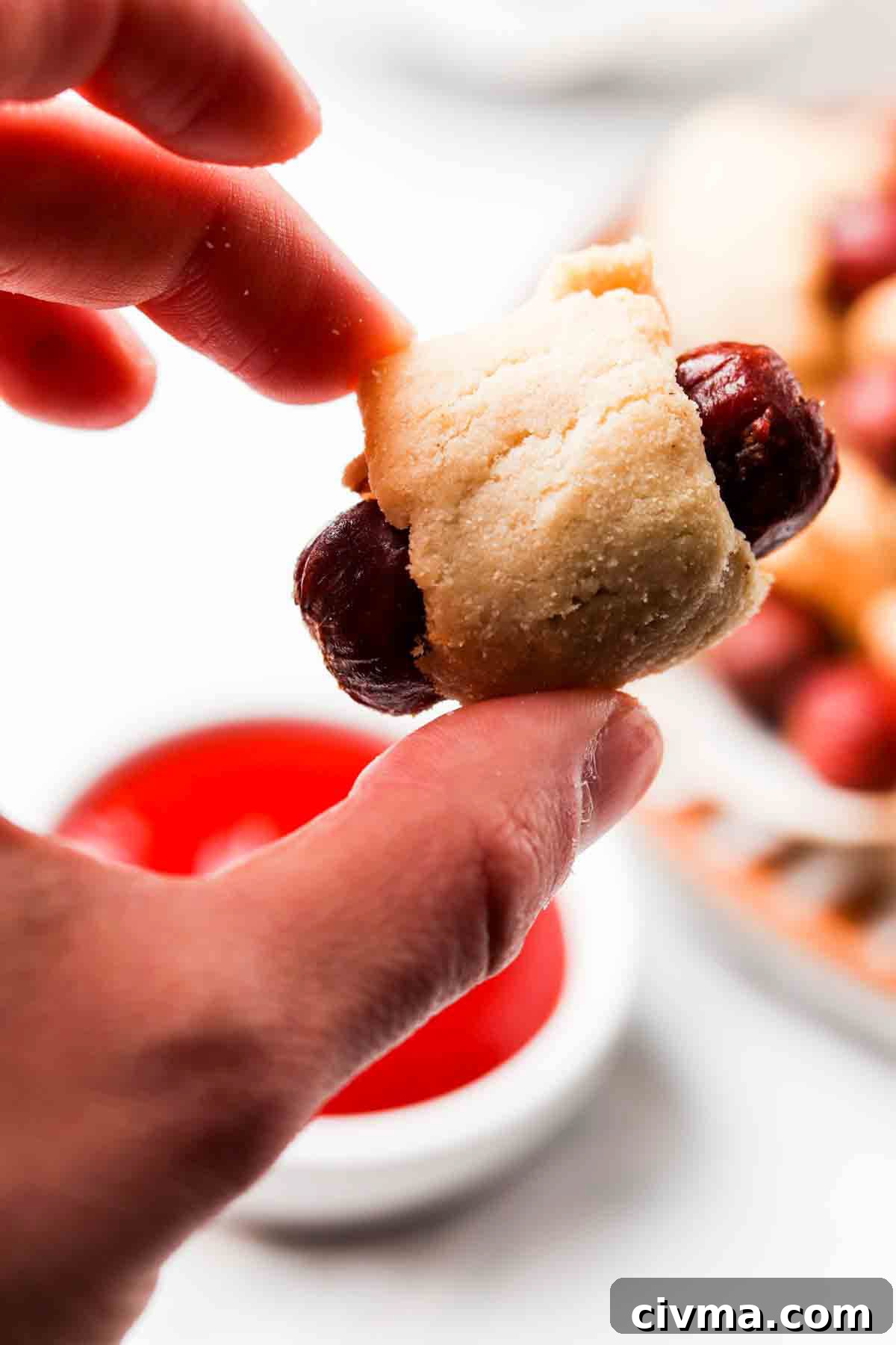 Hand holding a mini sausage wrapped in breading.