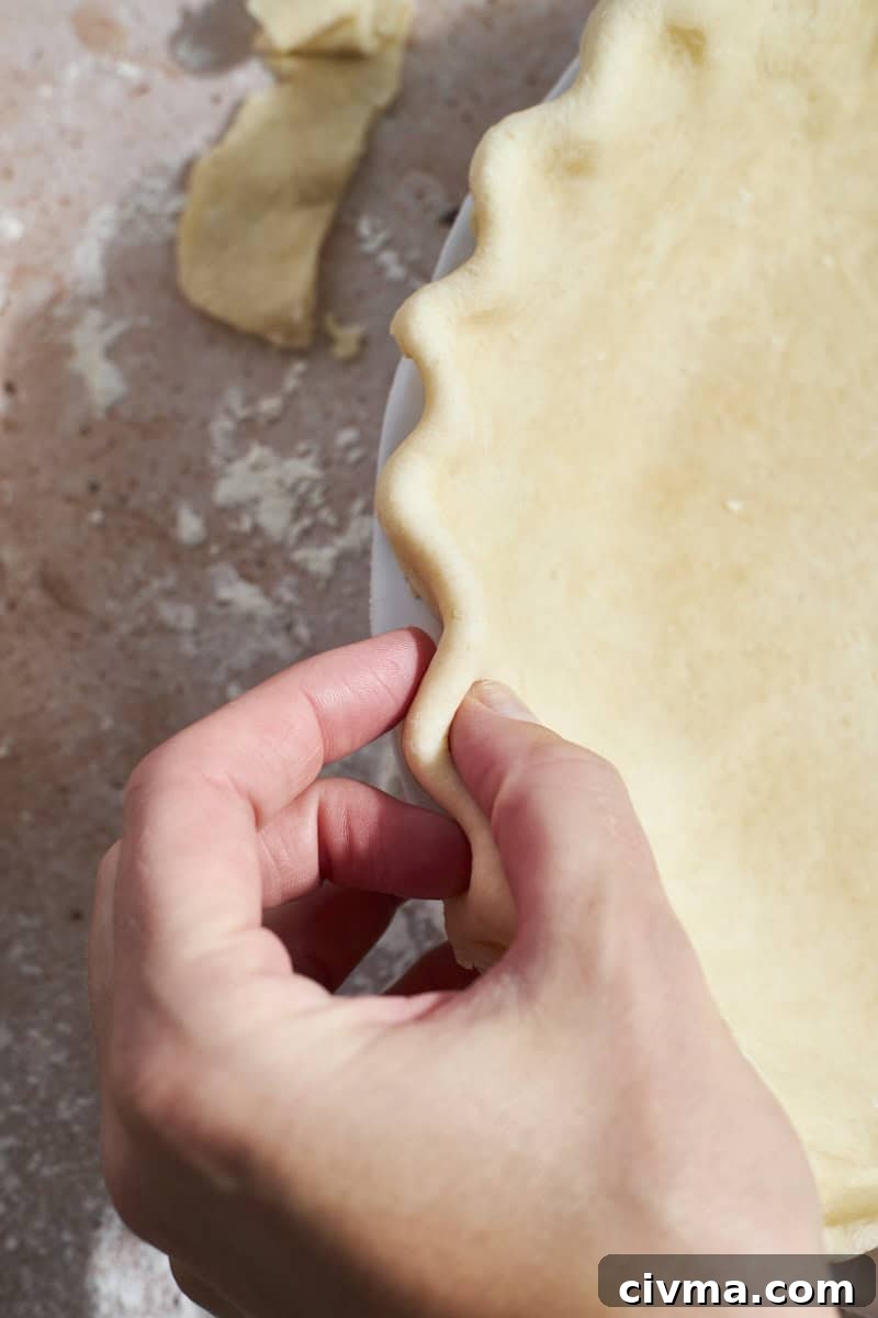 A hand crimping the edges of the pie crust.