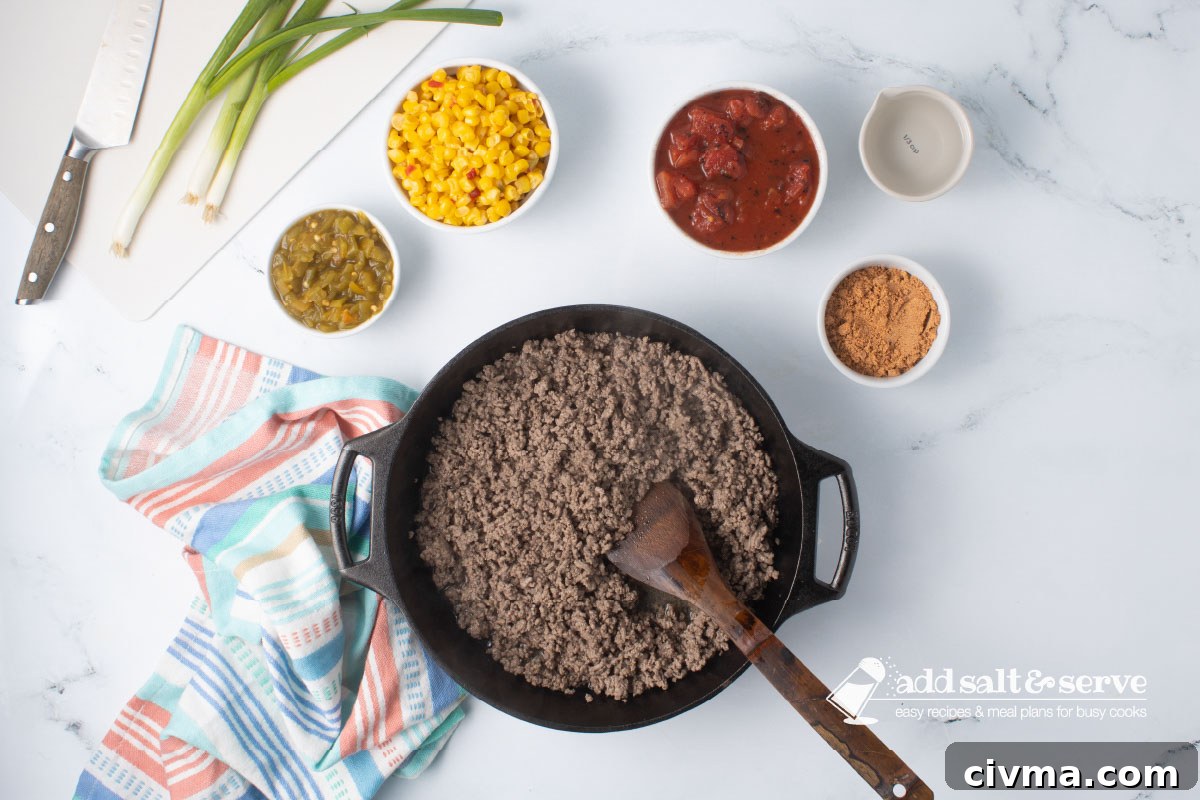 Cast iron skillet with cooked ground beef with a wooden spoon surrounded by bowls of green chilis, mexi-corn, fire-roasted diced tomatoes, taco seasoning, and water.