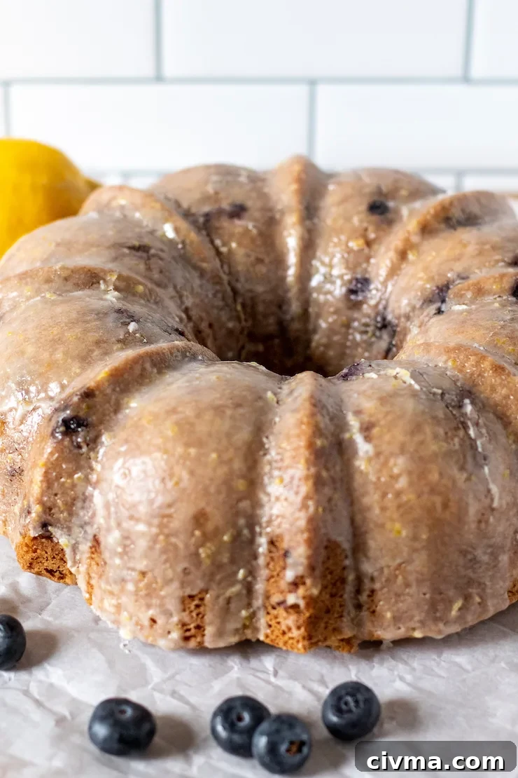 Glazed blueberry lemon cake with blueberries and lemon in background.