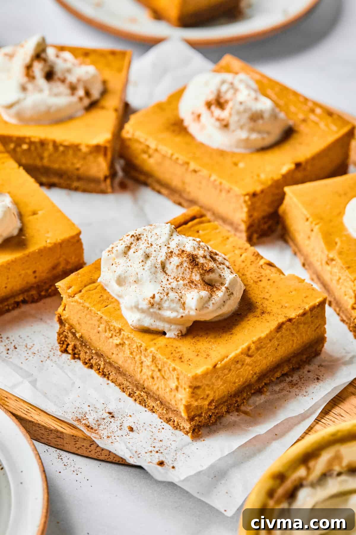 pumpkin cheesecake bars on parchment with whipped cream