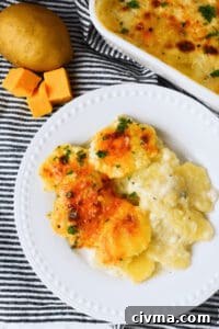 Plate of the side dish, garnished with herbs, next to cubes of cheddar and a whole potato, on a striped cloth.