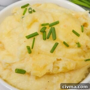 A bowl of creamy Cheesy Mashed Potatoes garnished with chopped chives.