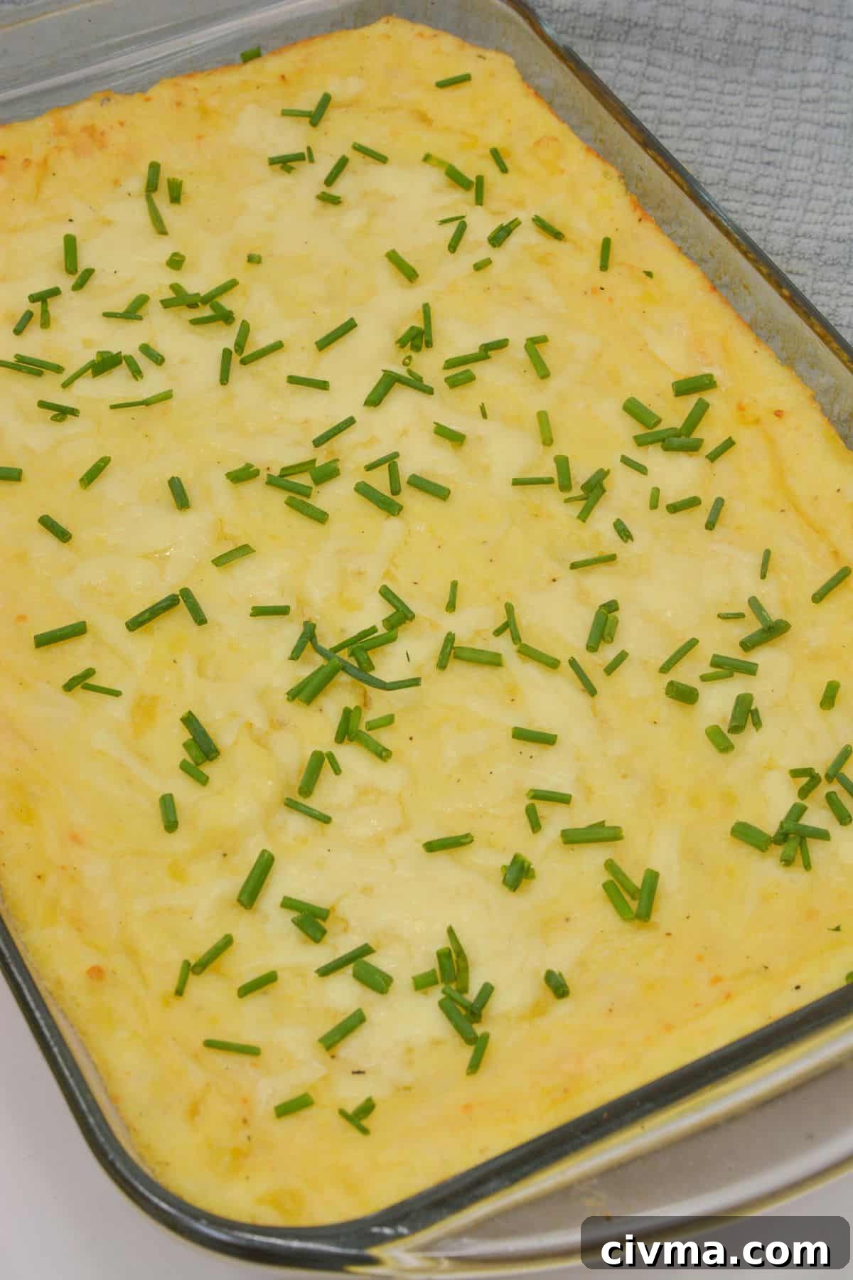 Casserole topped with chopped chives in a glass dish, resting on a gray textured cloth.