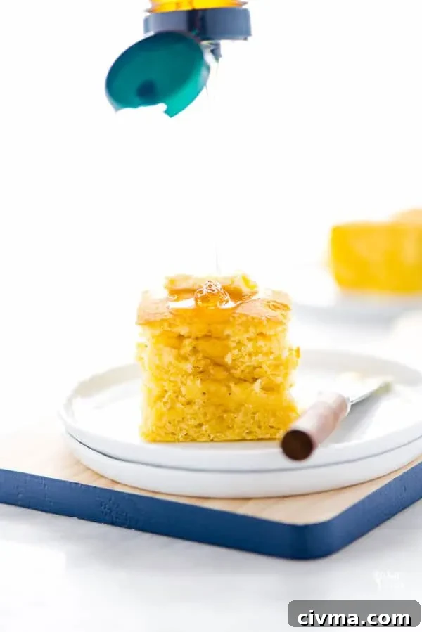 A piece of gluten free free sourdough cornbread on a stack of white plates topped with butter and being drizzled with honey