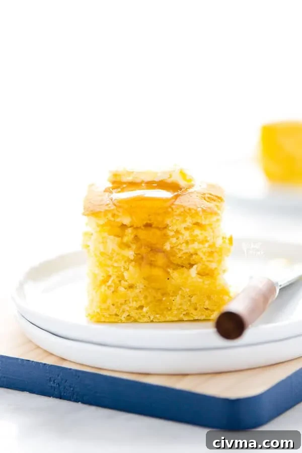 A piece of gluten free sourdough cornbread on a white plate topped with a pat of butter and honey