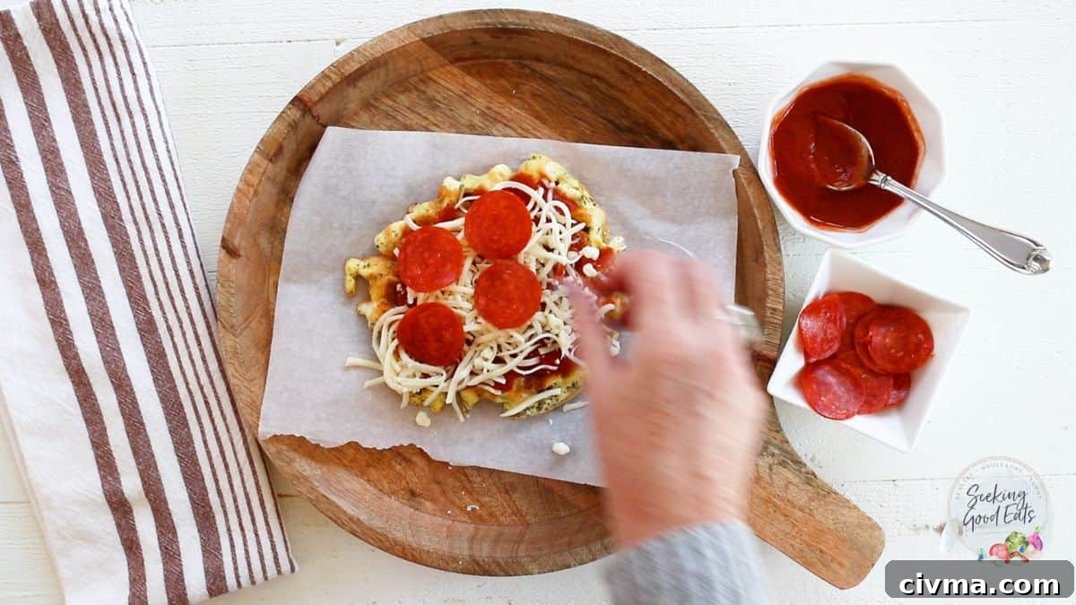 Adding pizza toppings to the top of a chaffle.