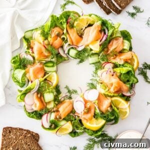 Smoked Salmon Wreath on a round white plate, sitting on a marble bench with some dressing and slices of rye bread around edge.