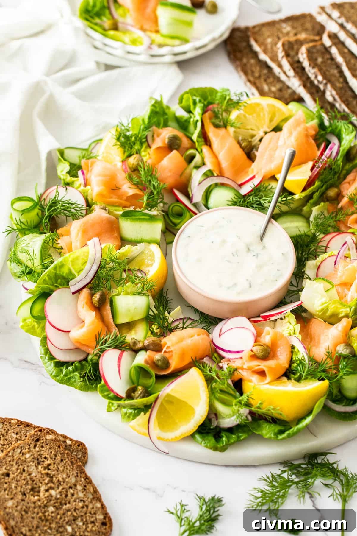 Smoked Salmon Wreath on a round white plate, with dish of dressing in centre of wreath and slices of rye bread around edge.