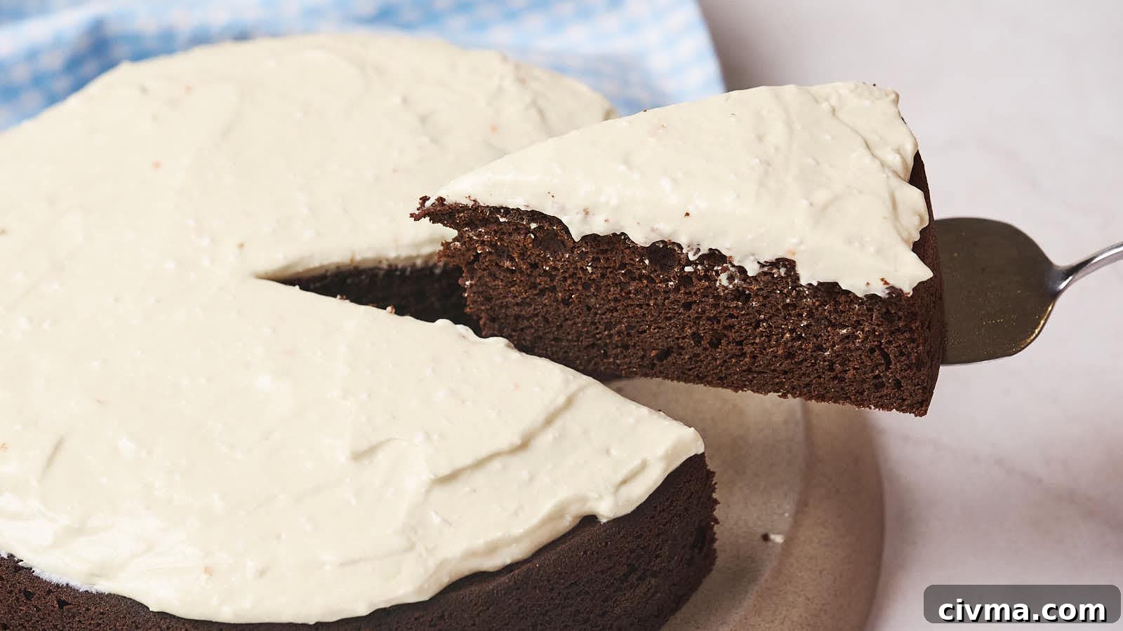 A slice of chocolate cake with white frosting being lifted from the whole cake.